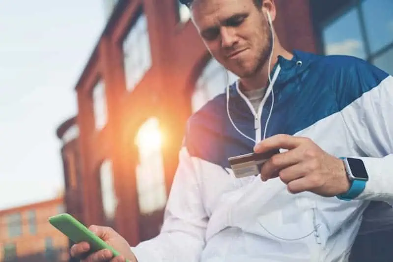 Man with credit card and mobile phone sitting on the street, web money and online payment