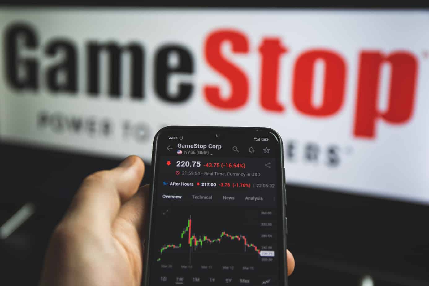 holding mobile phone with stock market charts of gamestop 213526229